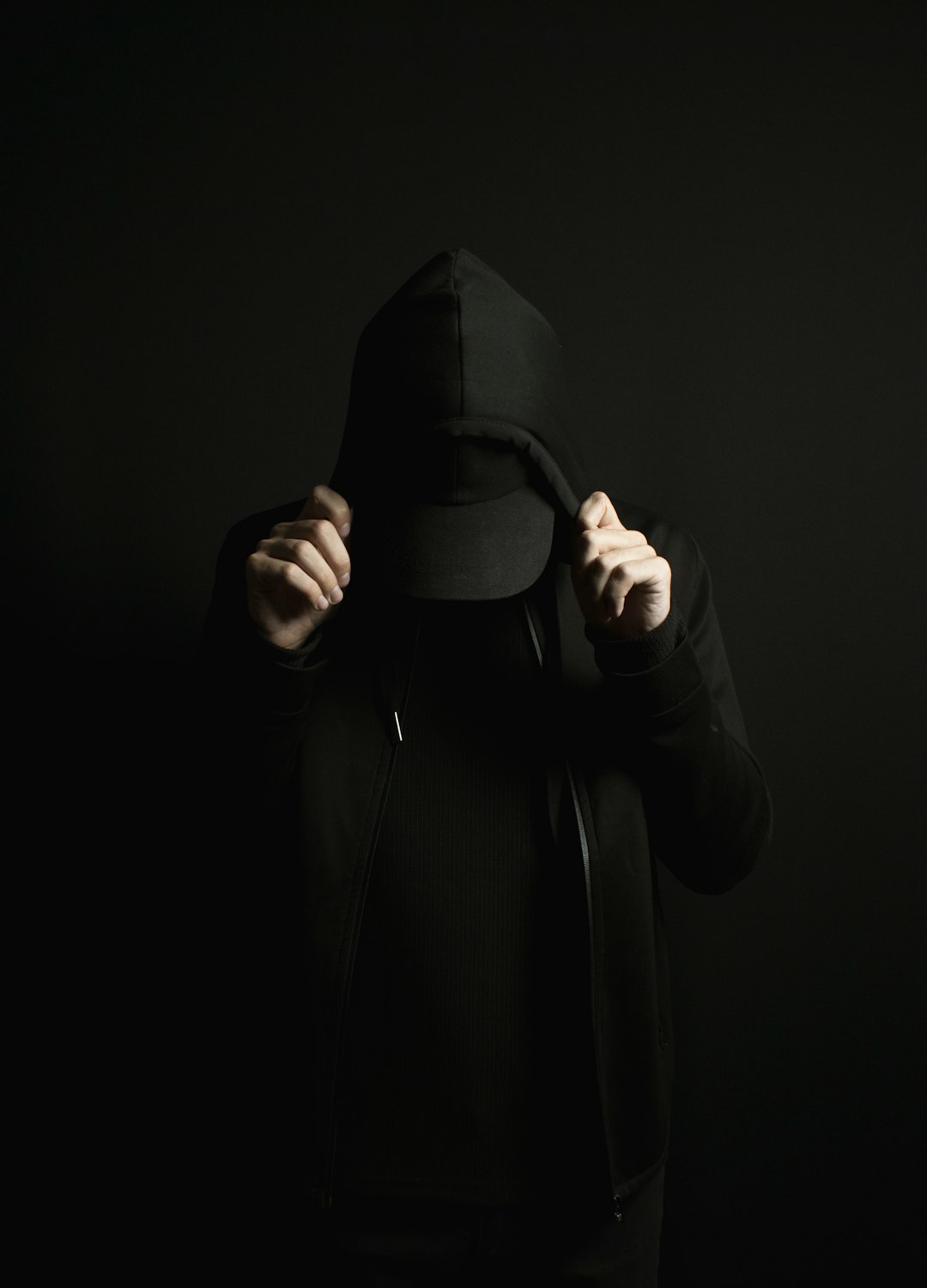 a person wearing a black hoodie and a black hat